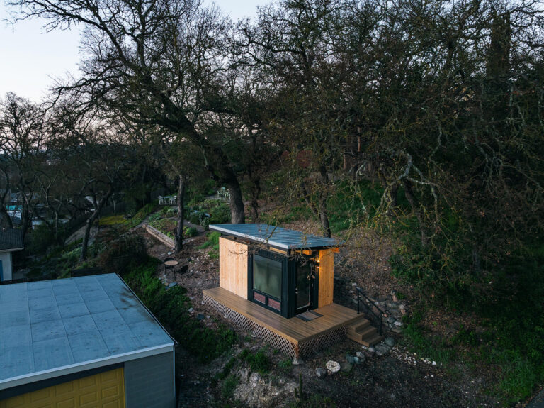 Modern prefab shed on hillside with deck and trees